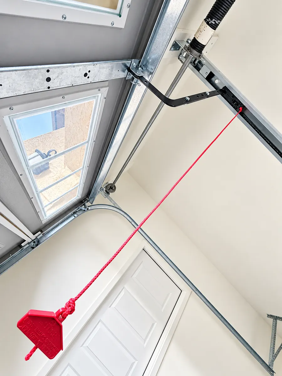 A red emergency release cord and handle hanging from the opener rail near the top of the garage door
