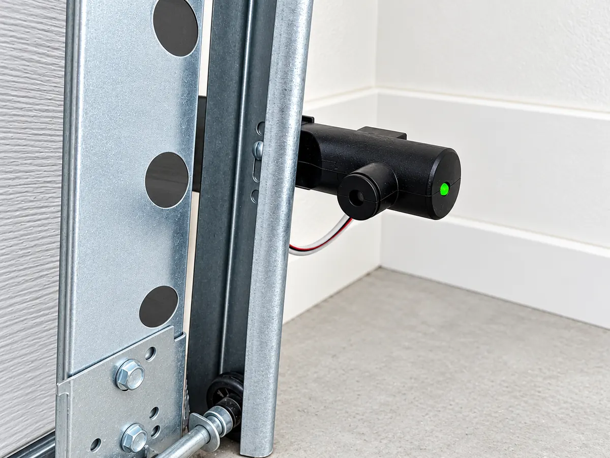 A safety sensor mounted on the door track a few inches above the garage floor, with its green light on